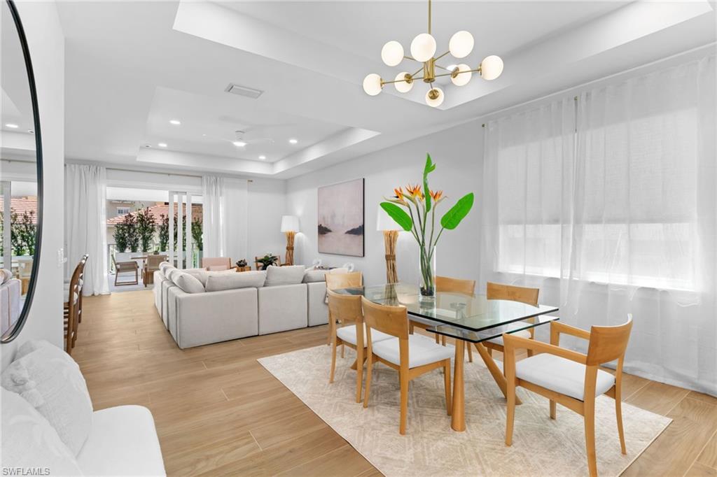 Open-concept living and dining area featuring wood-finish flooring, recessed lighting, and a tray ceiling