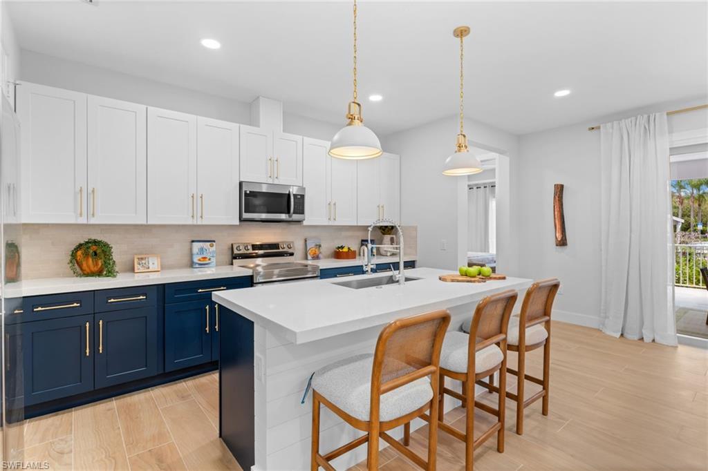 Modern kitchen featuring two-tone cabinetry with gold-finish hardware, stainless steel appliances, and a central island with a white countertop