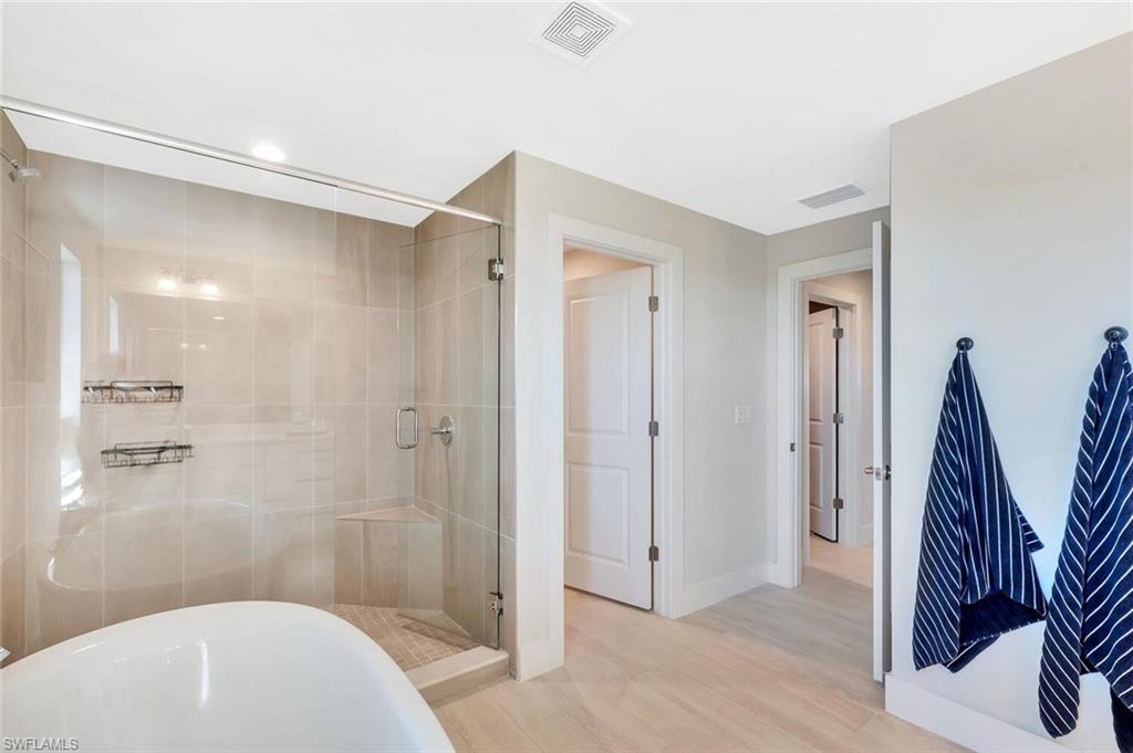 The primary bathroom at Preservation is a serene, spa-inspired retreat designed for both relaxation and refined daily living. A freestanding soaking tub anchors the space, creating a sculptural focal point that pairs beautifully with the expansive walk-in shower wrapped in floor-to-ceiling tile. The frameless glass enclosure and subtle neutral palette enhance the natural light, giving the room an airy, calming feel.Clean lines and warm textures carry through to the double entry doors and light wood-look
