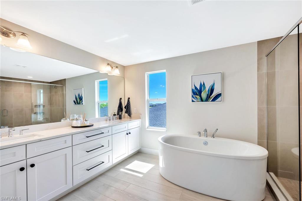 The primary bathroom at Preservation is a serene, spa-inspired retreat designed for both relaxation and refined daily living. A freestanding soaking tub anchors the space, creating a sculptural focal point that pairs beautifully with the expansive walk-in shower wrapped in floor-to-ceiling tile. The frameless glass enclosure and subtle neutral palette enhance the natural light, giving the room an airy, calming feel.Clean lines and warm textures carry through to the double entry doors and light wood-look