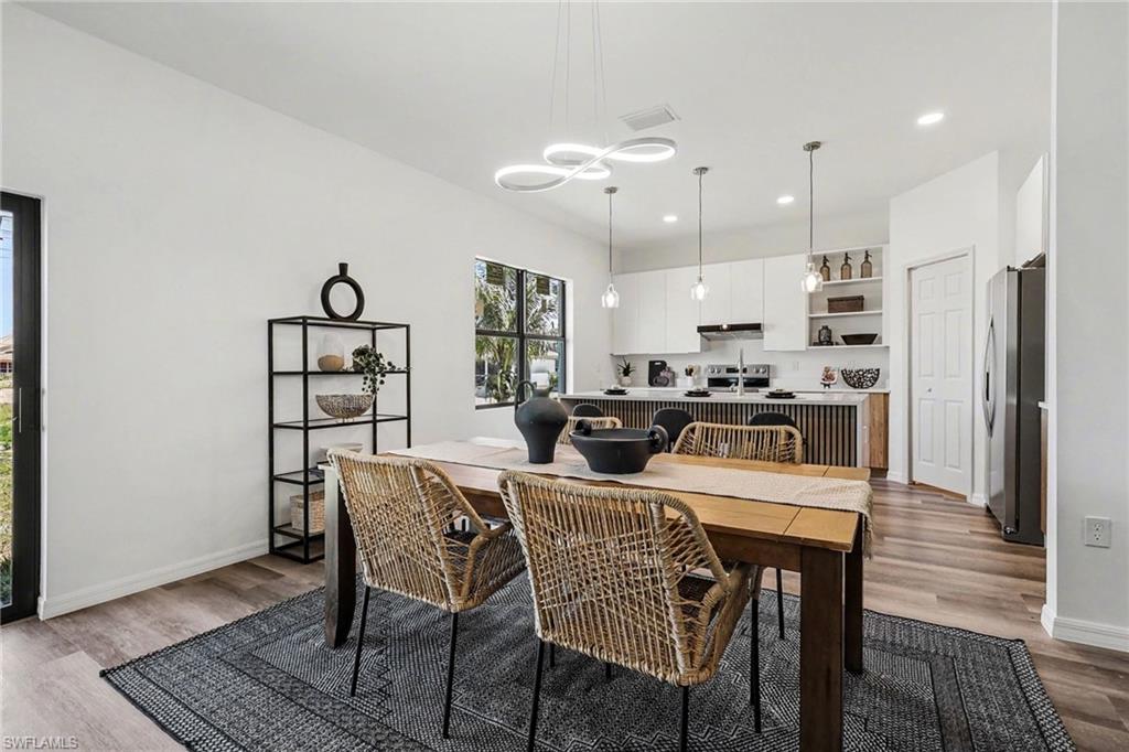 Open-concept dining area featuring wood-finish flooring, a contemporary chandelier, and a large window