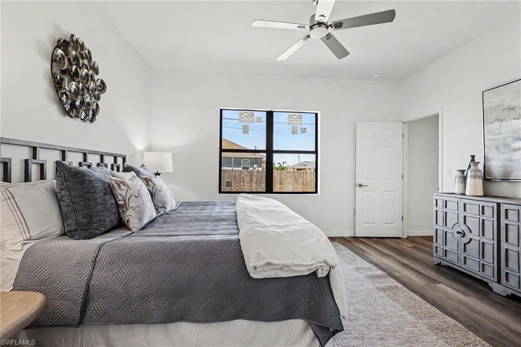 Spacious room featuring wood-finish flooring, a contemporary ceiling fan, ample natural light from a large window, a white paneled door, and a decorative headboard