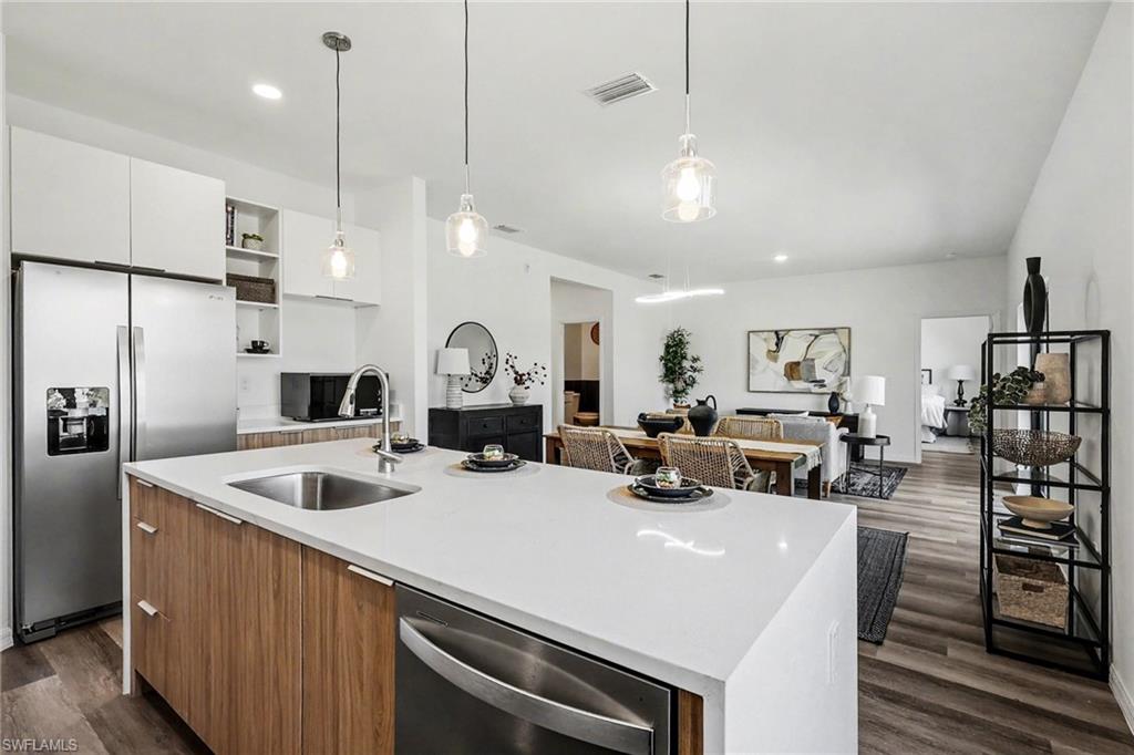 Open-concept living space with a kitchen island featuring a stainless steel sink, wood-finish cabinetry, and a dishwasher