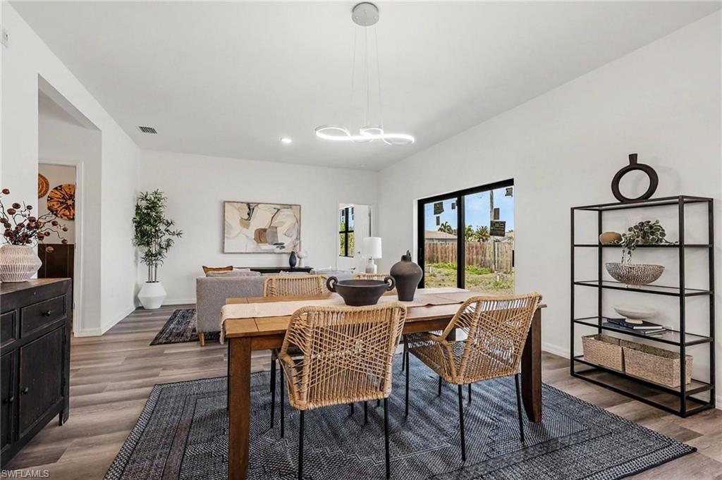 Open-concept living space featuring wood-finish flooring, white walls, a linear pendant light fixture, recessed ceiling lighting, and a large sliding glass door