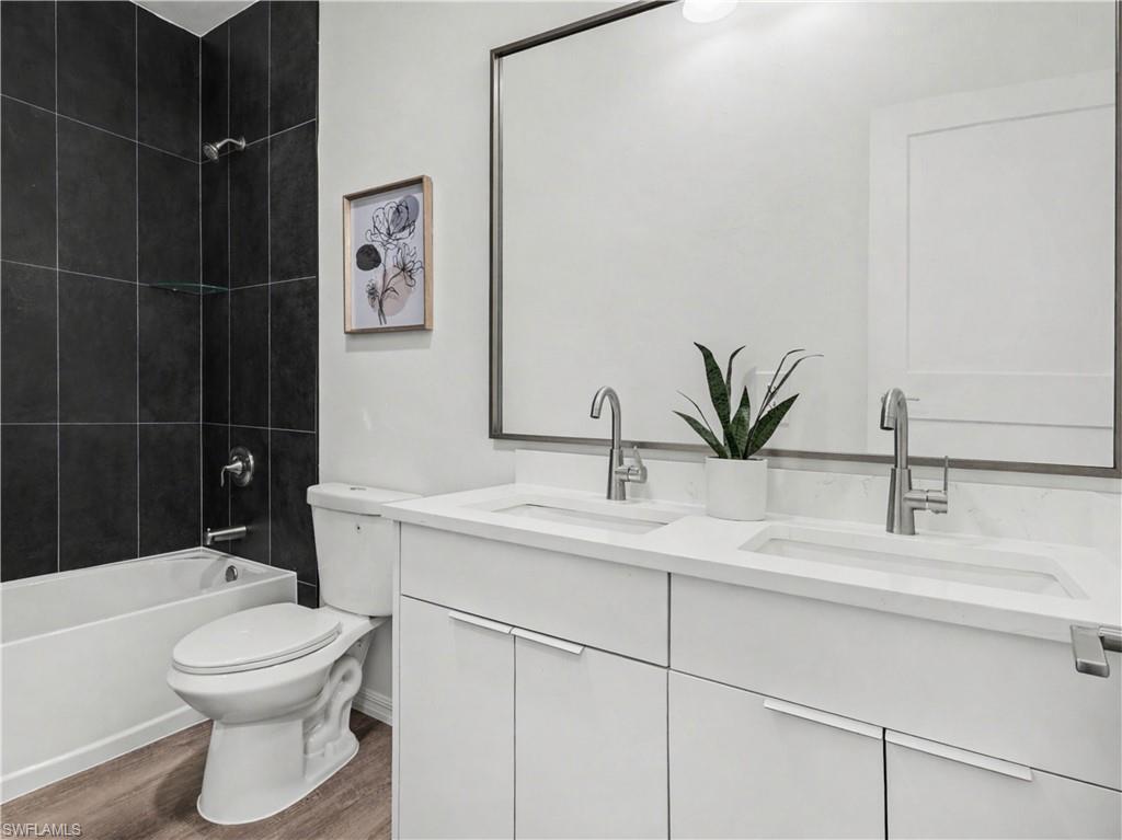 Bathroom with a dual vanity, white cabinetry, integrated sinks, a wide mirror, virtually added, and wood-finish flooring