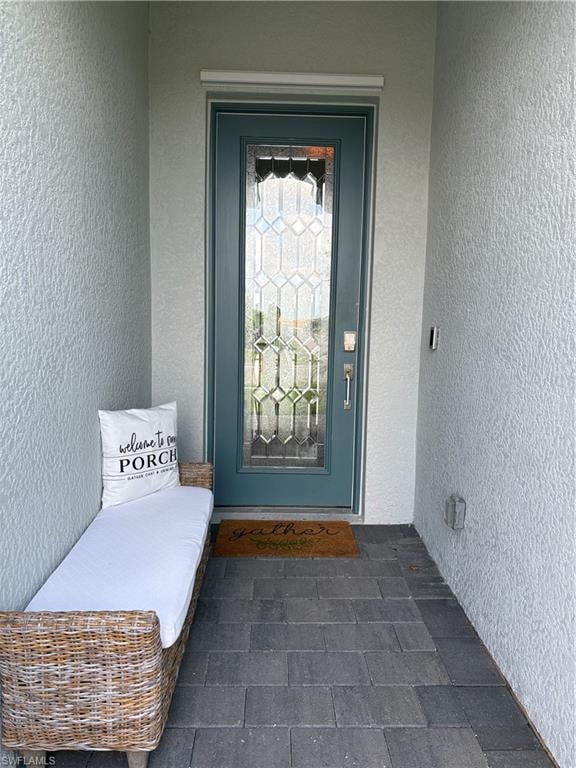 Entryway featuring a decorative glass panel door with sidelights, textured exterior walls, and dark gray paver flooring