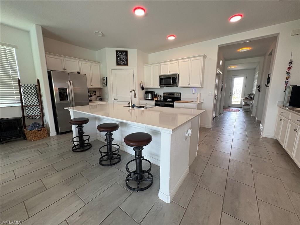 Spacious kitchen featuring an expansive central island with countertop seating, white shaker cabinetry, stainless steel appliances, and large format tile flooring