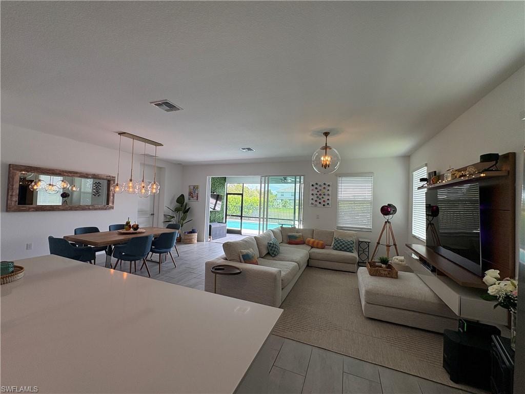 Open-concept living area with a contemporary linear chandelier over the dining space, a large mirrored wall accent, and tile flooring