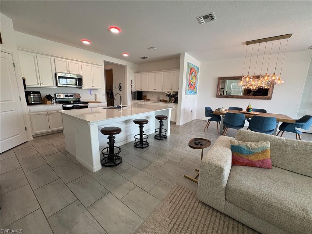 Open-concept kitchen and dining area featuring a large center island with seating, extensive white cabinetry, stainless steel appliances, and light-toned tile flooring