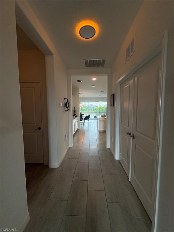 Hallway featuring plank-style tile flooring, white baseboards, and a contemporary ceiling light fixture