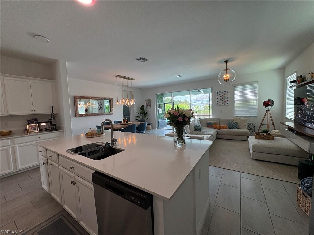 Open-concept kitchen and living area featuring a large center island with an undermount sink, white cabinetry, stainless steel dishwasher, and tile flooring