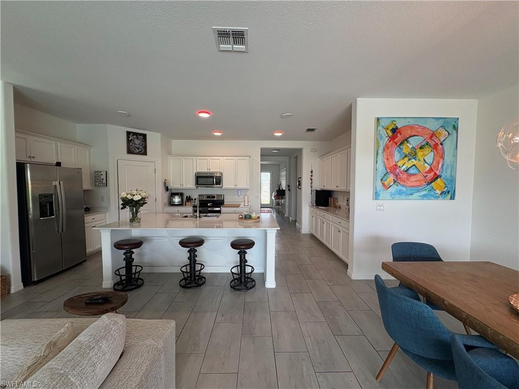 Spacious kitchen featuring an extended island with a light-toned countertop, white cabinetry, recessed lighting, and stainless steel appliances