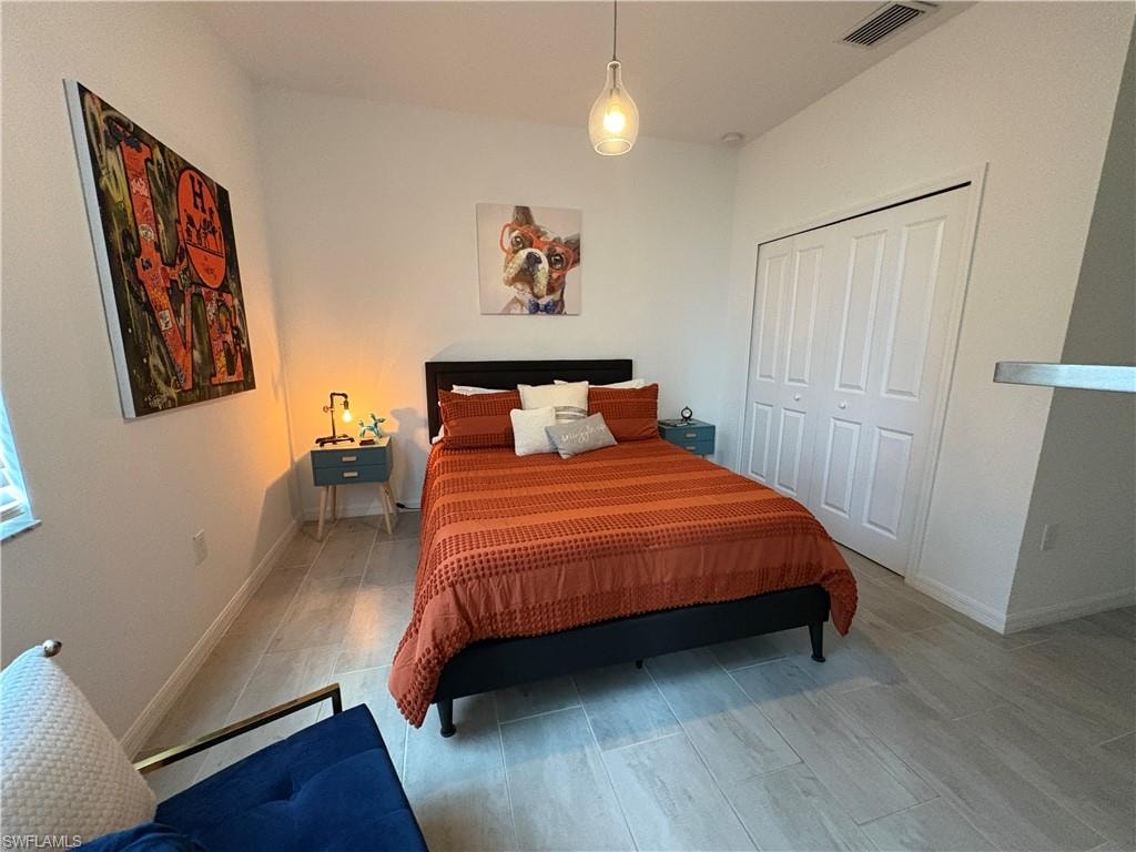 Bedroom featuring light-toned plank tile flooring, a built-in closet with bi-fold doors, a single pendant light fixture, and white baseboards