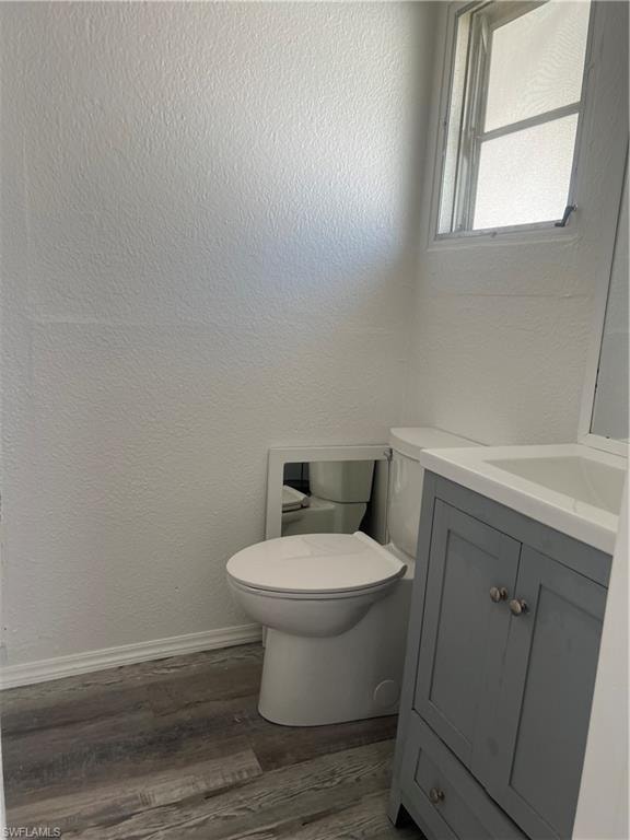 Half bathroom featuring baseboards, wood finished floors, vanity, and toilet
