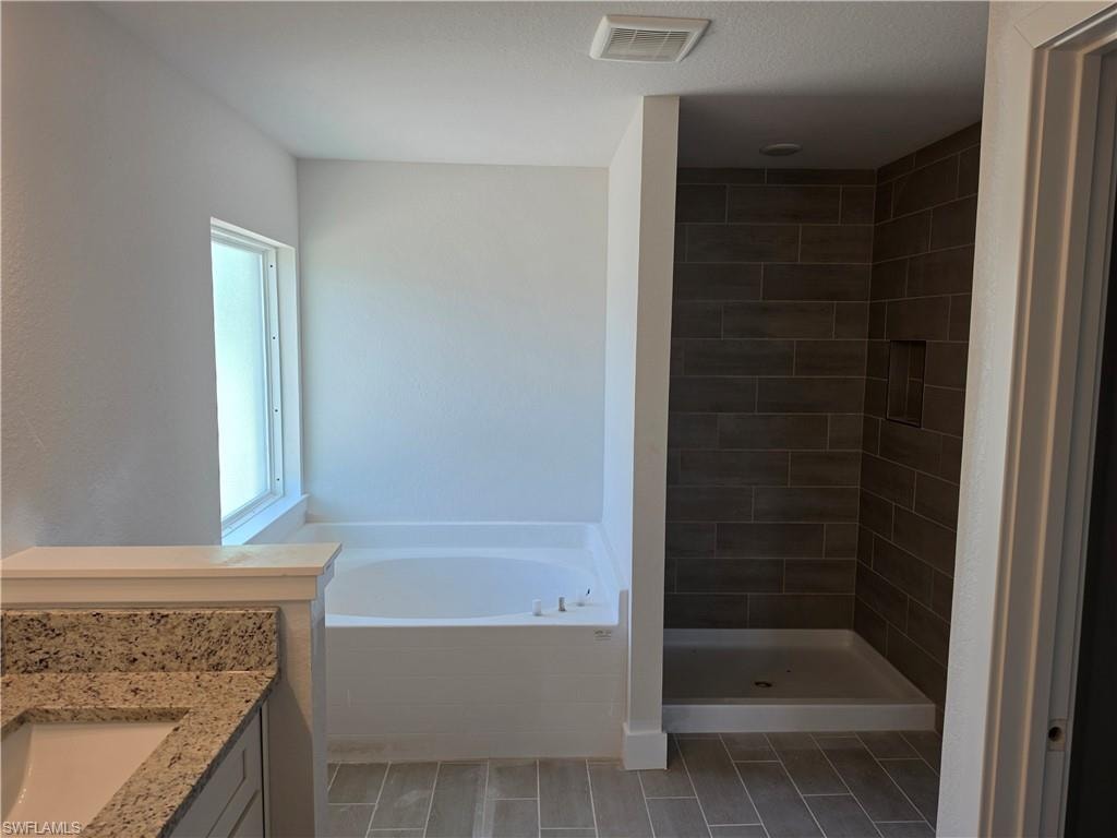 Bathroom featuring a built-in tub, a walk-in shower with tiled walls and a recessed niche, wood-finish tile flooring, a window, and a vanity with a granite countertop and an undermount sink
