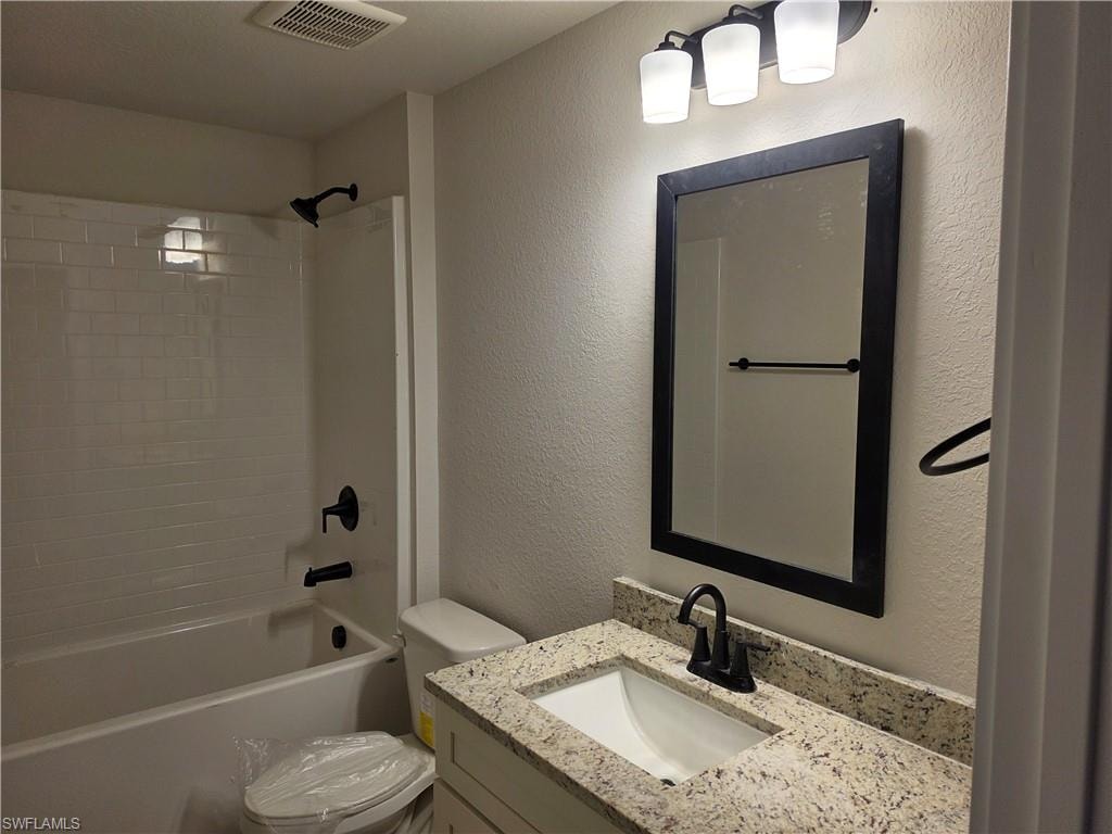 Bathroom featuring a white subway tile shower surround with matte black fixtures, a built-in bathtub, and a vanity with a light-colored speckled countertop