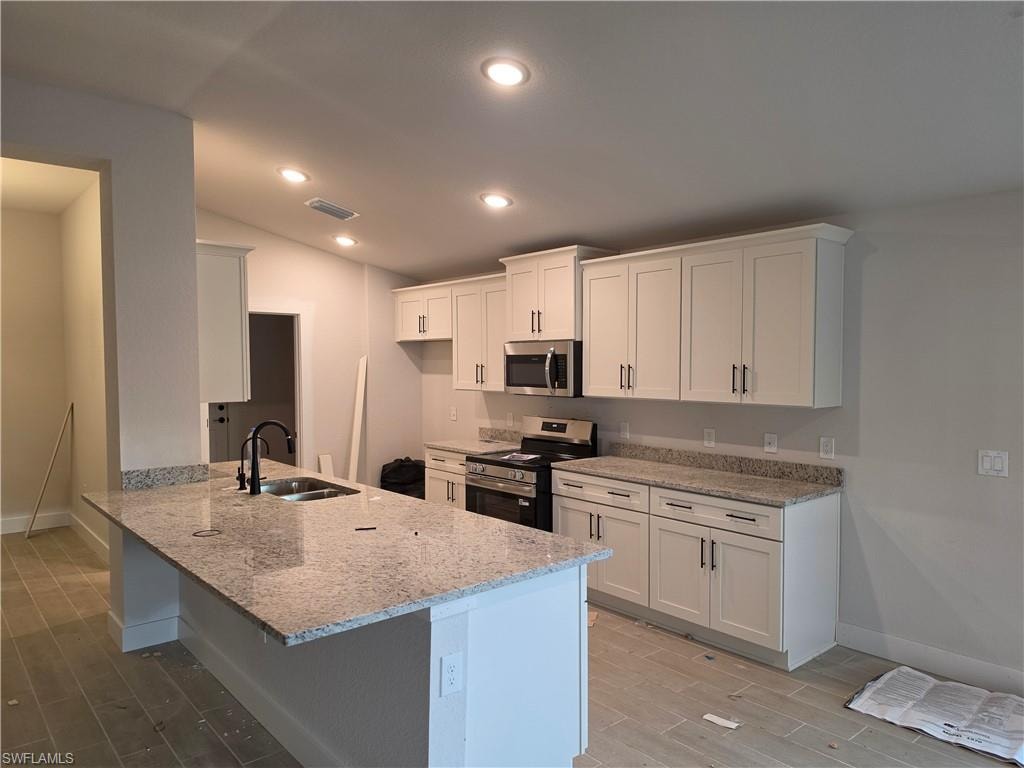Kitchen featuring light-toned cabinetry, stainless steel appliances, granite countertops, and a central island with an undermount sink