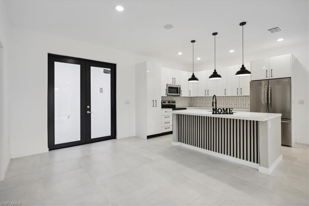 Modern kitchen featuring white shaker cabinetry, stainless steel appliances, a center island with sink, dark wood-finish backsplash, and light tile flooring