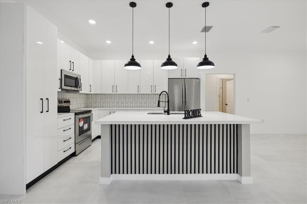 Modern kitchen featuring white shaker cabinetry, stainless steel appliances, a center island with contrasting wood-finish paneling, dark wood-finish backsplash, and three pendant lights