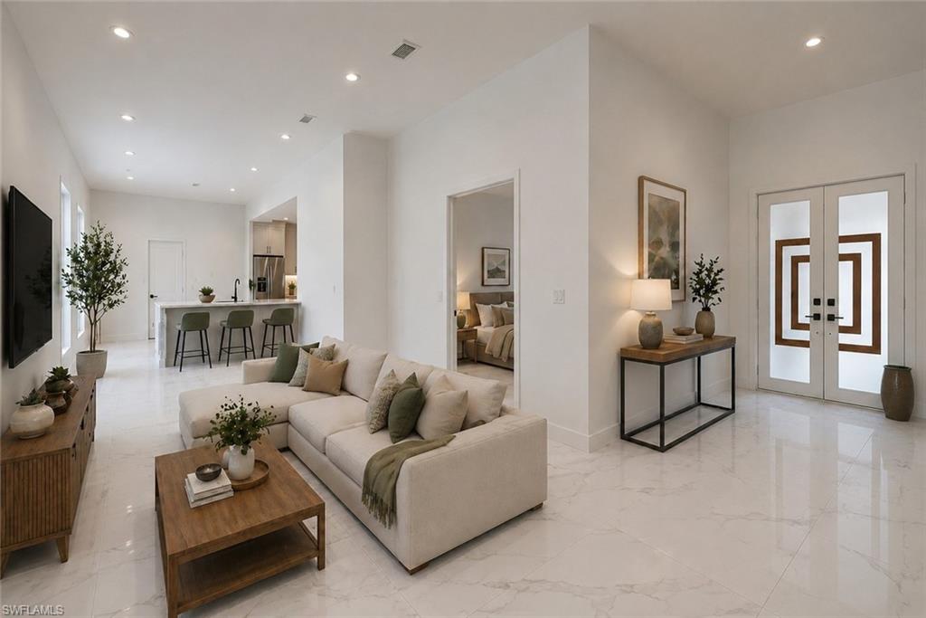 Bright living area featuring white tile flooring, recessed lighting, and a kitchen pass-through with a breakfast bar. Image digitally enhanced and virtually altered; actual property condition may differ.