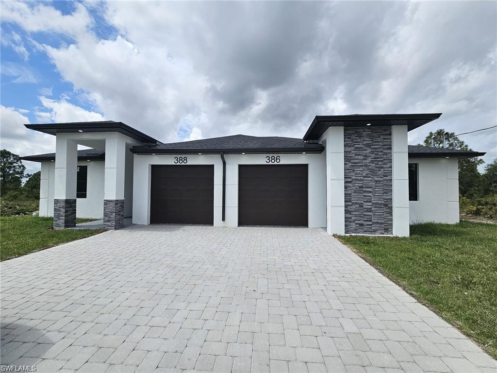 View of front of property with an attached garage, stone siding, stucco siding, and decorative driveway