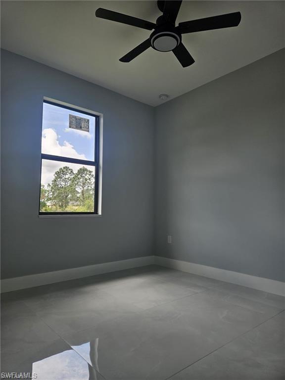 Empty room with concrete flooring, baseboards, and ceiling fan