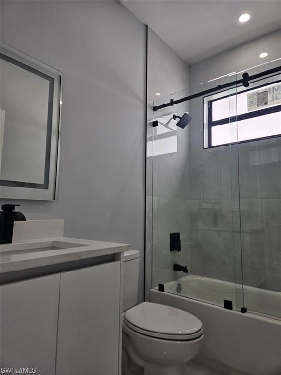 Bathroom with toilet, vanity, and enclosed tub / shower combo