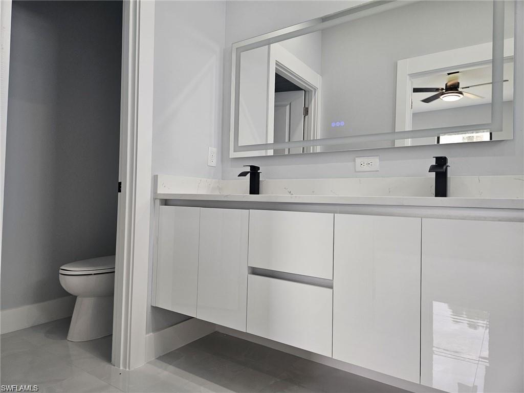 Full bathroom with double vanity, toilet, ceiling fan, and baseboards