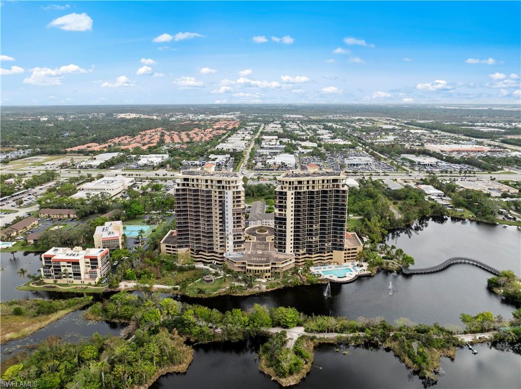 Aerial view of the property and its surrounding area, featuring two high-rise buildings, a large body of water, and lush green landscaping