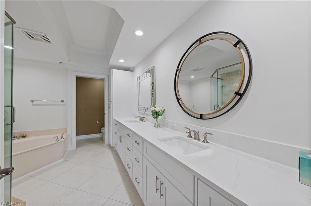 The bathroom features a double vanity with white cabinetry and countertops, a large round mirror with a dark frame, and a corner bathtub