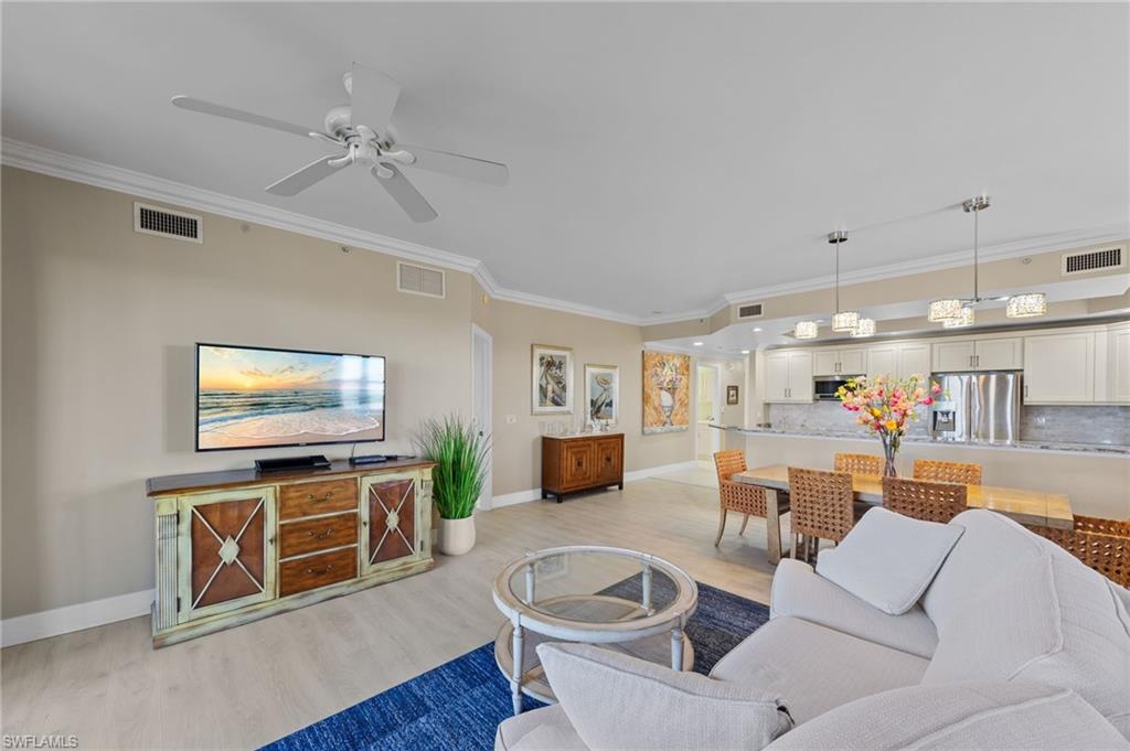 The expansive living area features a ceiling fan, light-toned flooring, and crown molding
