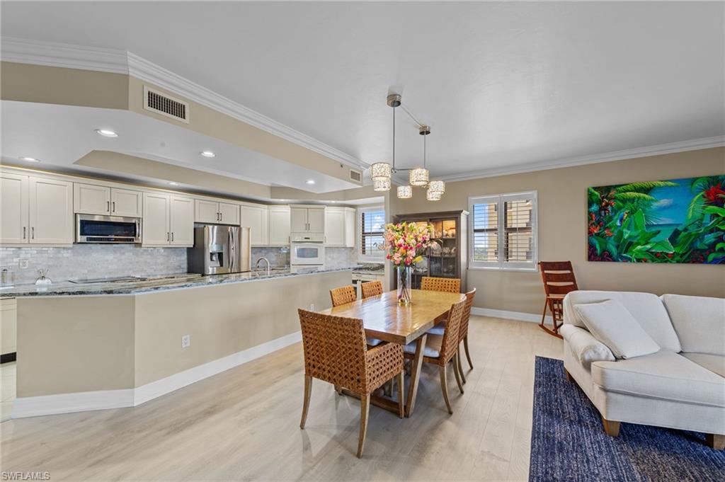 Open concept living space featuring light-toned flooring, recessed lighting, and a modern kitchen with a breakfast bar, light cabinetry, stainless steel appliances, and a tiled backsplash
