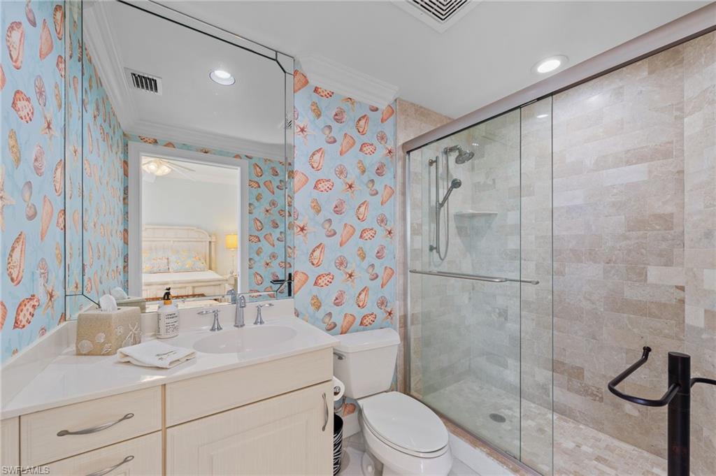 Bathroom featuring a vanity with a white countertop and double-door storage, a toilet, and a glass-enclosed shower with tile walls