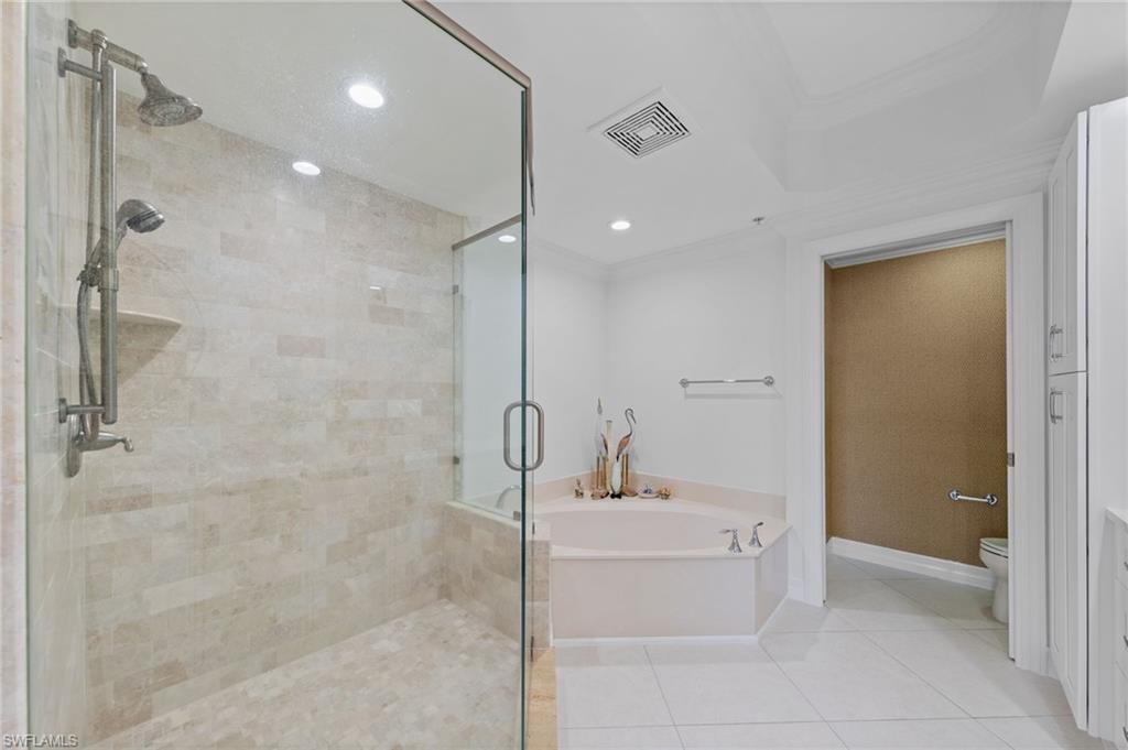 The bathroom features a spacious glass-enclosed shower with tiled walls and a handheld showerhead