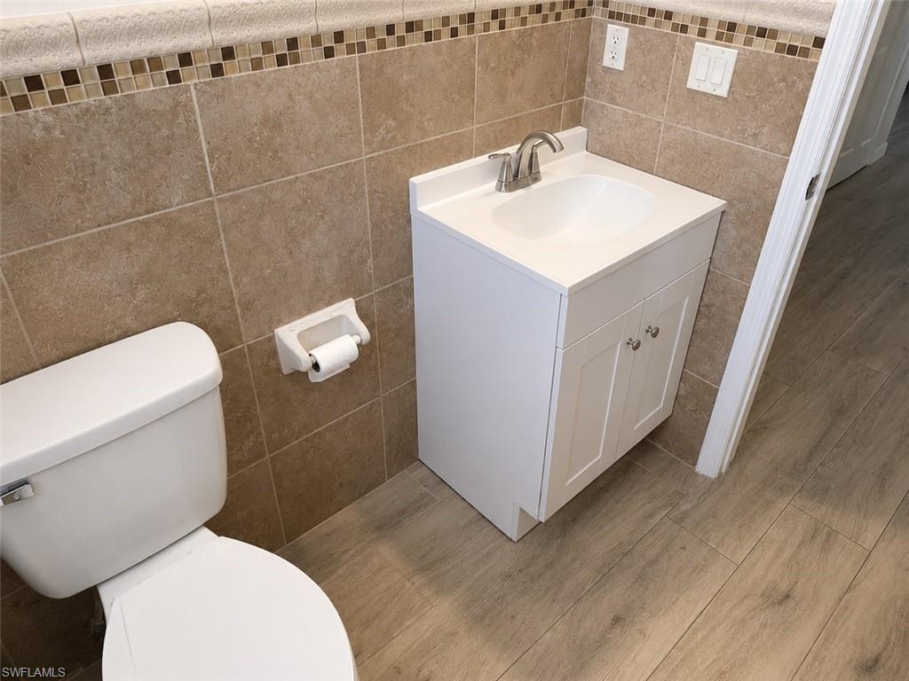 Bathroom featuring a white toilet, floor-to-ceiling tiled walls with decorative mosaic accent, and a white vanity with an integrated sink and brushed nickel faucet