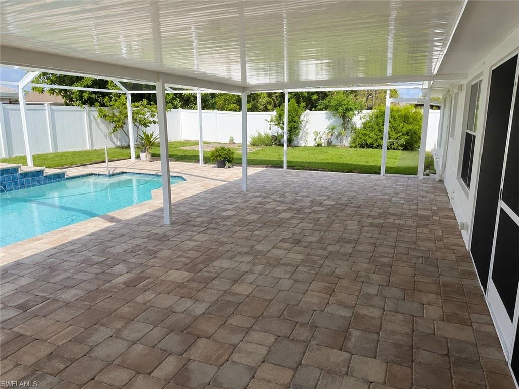 Covered patio featuring multi-toned paver flooring, a refreshing swimming pool with tiled steps, and a white privacy fence encompassing the backyard
