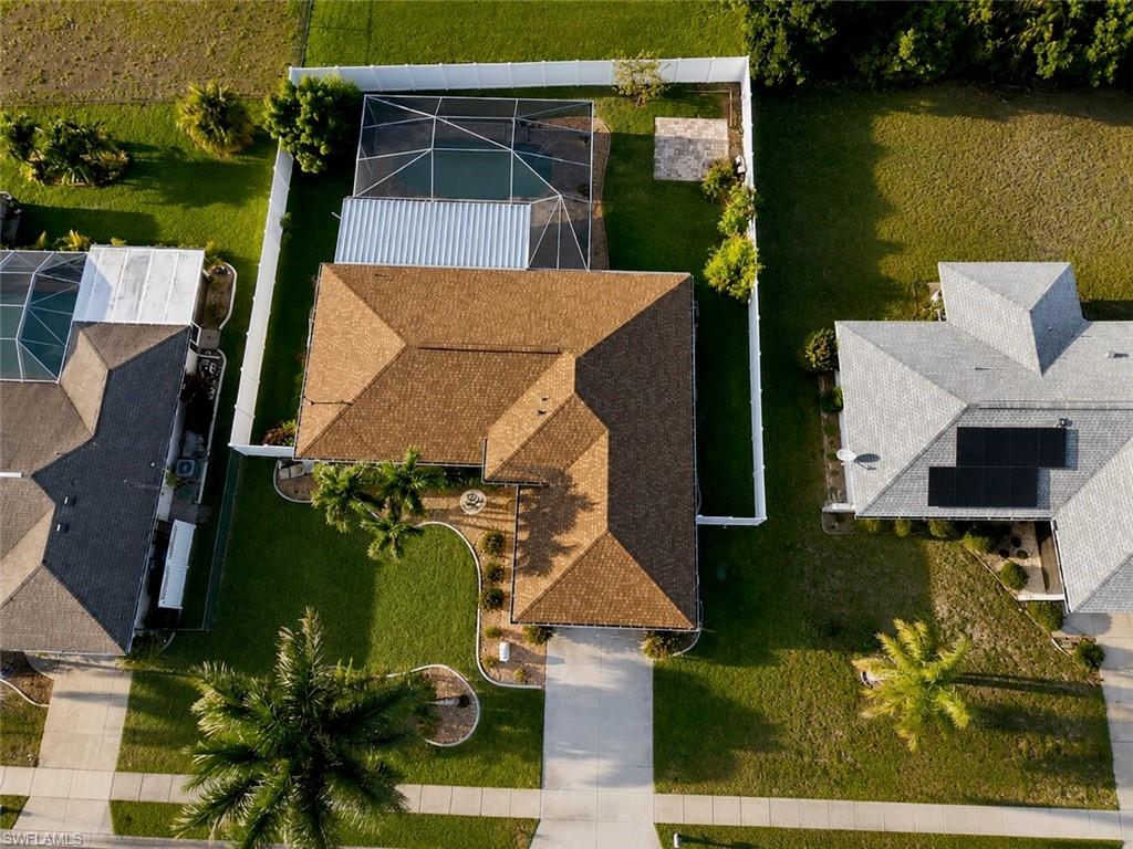 Aerial perspective showcasing a property with a brown shingle roof, concrete driveway, and established front yard landscaping