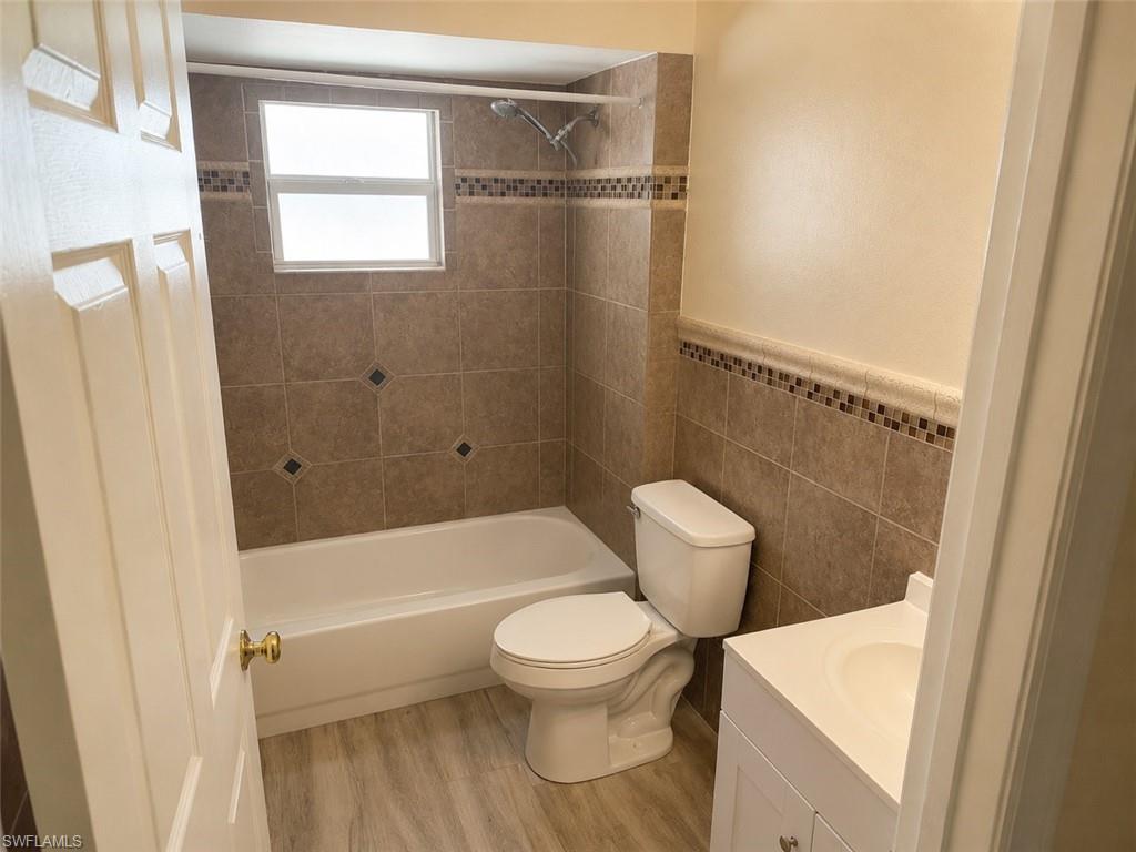 Full bathroom featuring an integrated bathtub and shower with brown tile surround, a white vanity with integrated sink, and wood-finish flooring