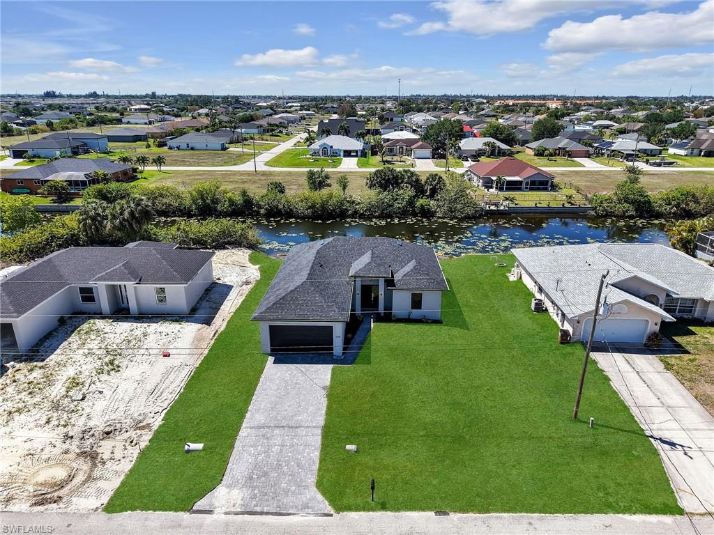 Newly constructed residence featuring a dark shingle roof, paver driveway, and a spacious green lawn  the color of the grass has been virtually enhanced