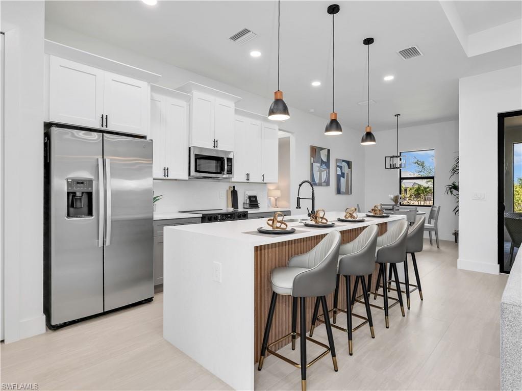 Modern kitchen featuring white shaker cabinetry, stainless steel appliances, a center island with pendant lighting, a black gooseneck faucet, and light wood-finish flooring photos used from another listing to show what it would look like with furniture