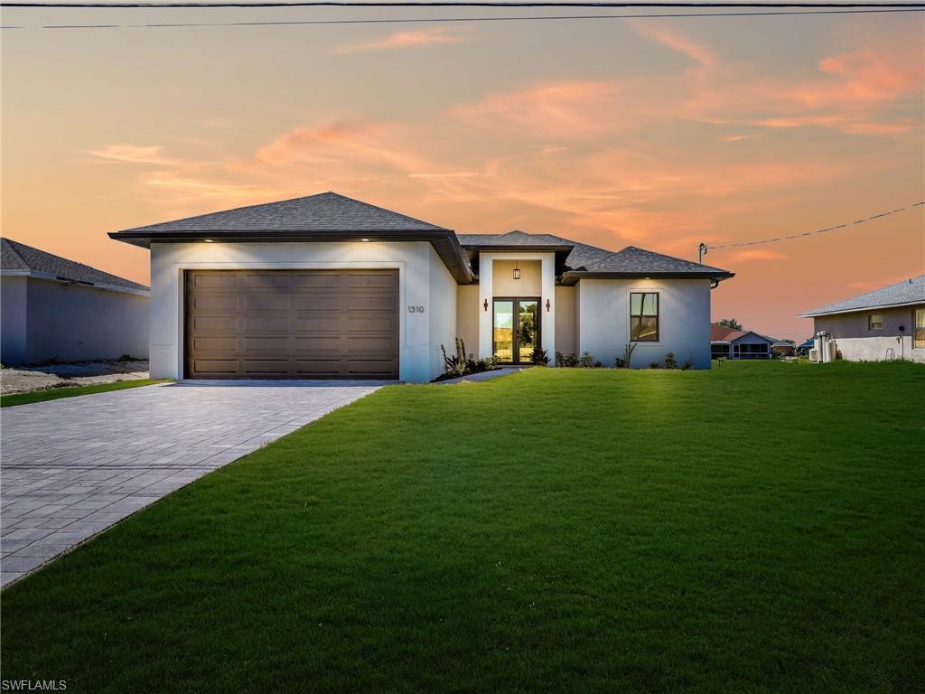 Contemporary stucco exterior with a dark brown garage door, dark shingle roof, and a paved driveway  the color of the grass has been virtually enhanced