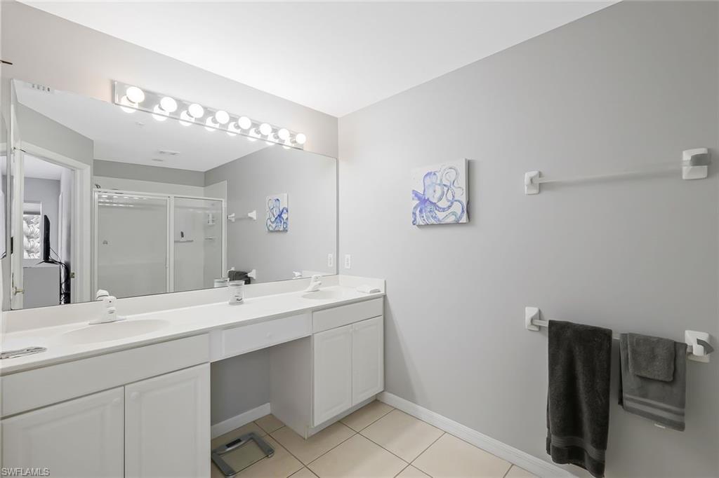 Bathroom with an enclosed shower, tile flooring, vanity with extensive cabinet space, and dual sinks
