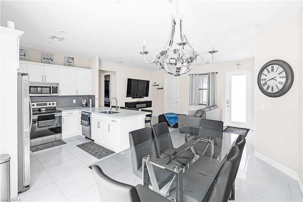 Open-concept living area featuring a modern kitchen with white cabinetry, stainless steel appliances, a center island with sink, and a gray subway tile backsplash