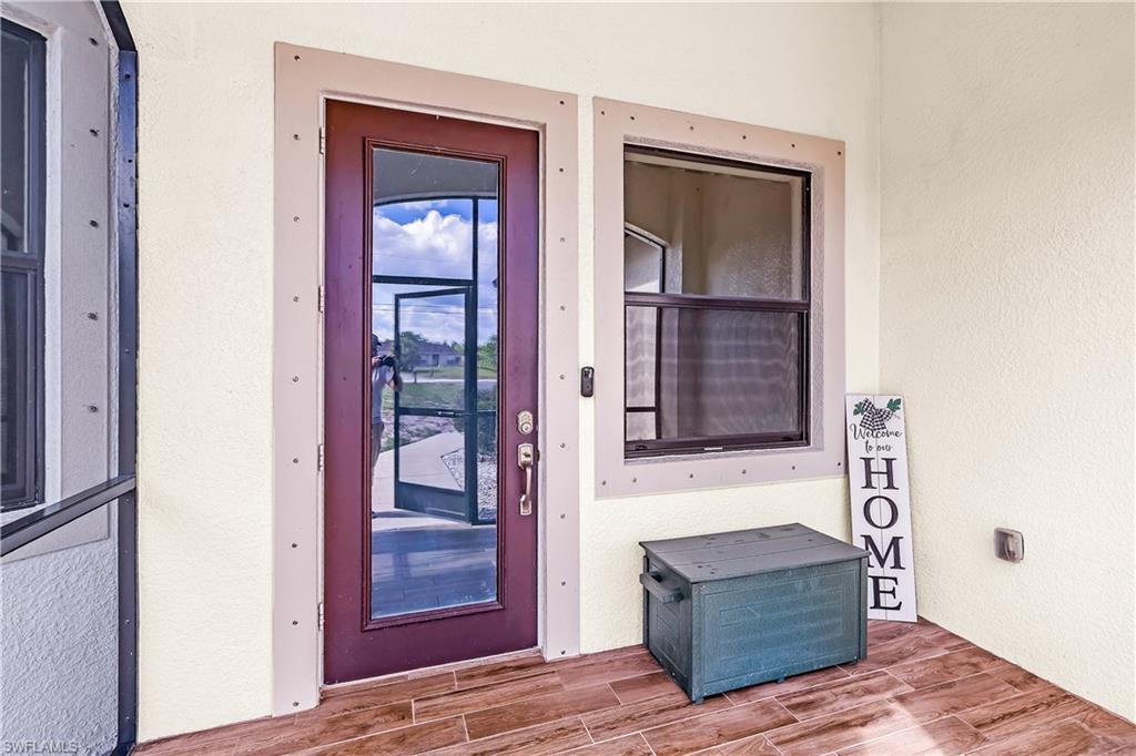 Entryway featuring a rich wood-finish door with glass paneling, durable wood-finish tile flooring, textured exterior wall finish, and an exterior window with a screen