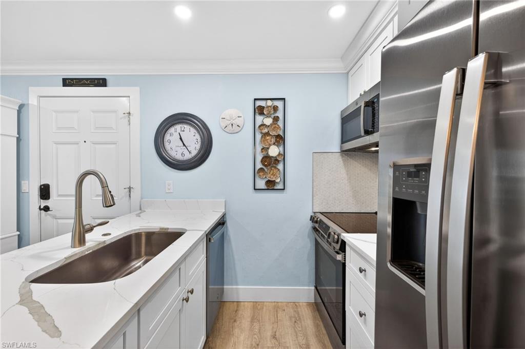 Kitchen featuring white cabinetry, a large stainless steel sink with a gooseneck faucet, light-toned wood-finish flooring, white countertops with veining, and stainless steel appliances