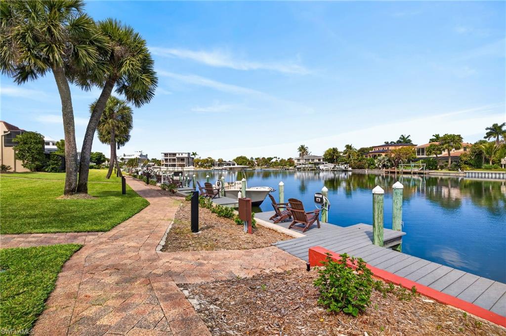 Waterfront property featuring a community dock with pilings, a paved pedestrian pathway, and mature palm trees
