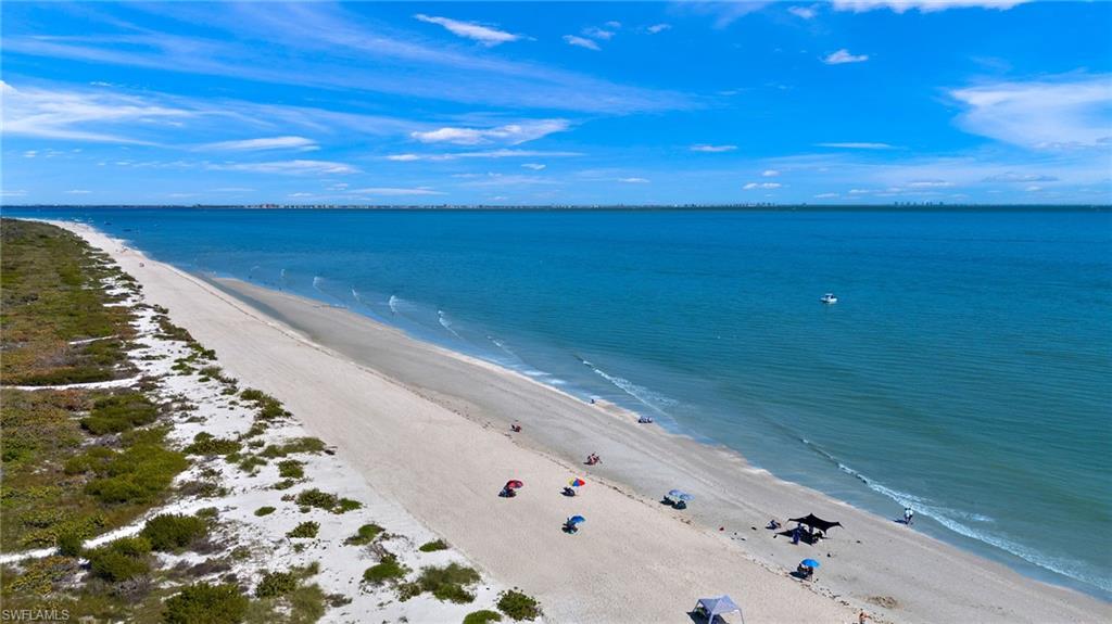 Expansive sandy beach with coastal vegetation, calm blue water, and distant shoreline