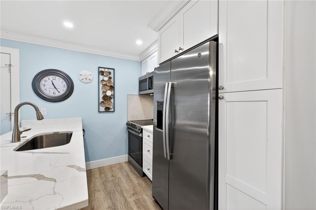 Kitchen featuring white shaker-style cabinetry, stainless steel appliances, light-toned countertops with veining, a stainless steel undermount sink, and wood-finish flooring