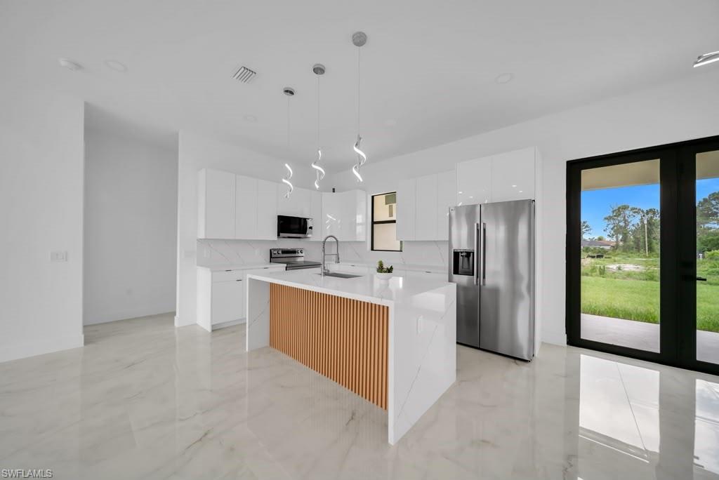 Modern kitchen featuring a waterfall island with wood-slat detailing, white cabinetry, integrated stainless steel appliances, and sleek pendant lighting