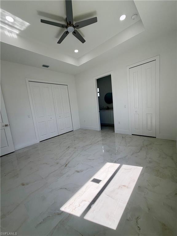 Spacious room featuring large format tile flooring, a tray ceiling with recessed lighting, and a ceiling fan